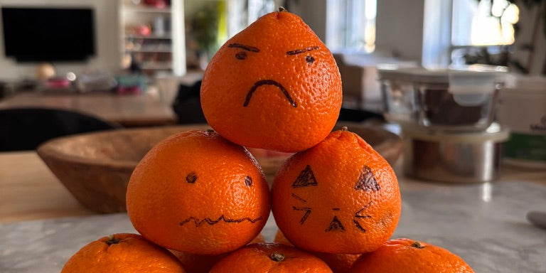 Six oranges stacked in a pyramid with hand-drawn Halloween faces on their peels.