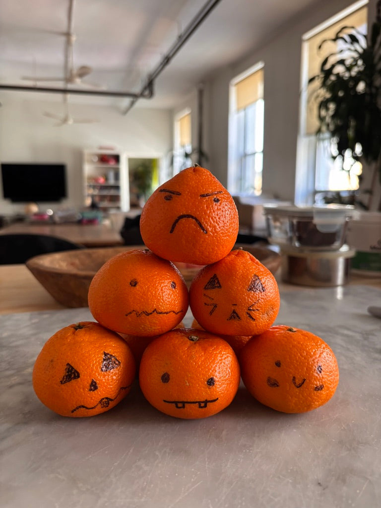 Six oranges stacked in a pyramid with hand-drawn Halloween faces on their peels.