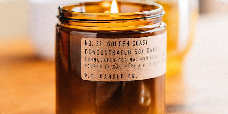 Lit P. F. Candle Co. Golden Coast candle in an amber glass jar on a wooden surface.