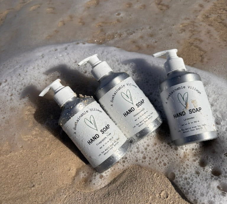 aluminum bottles of hand soap on a sandy surface with water and foam.