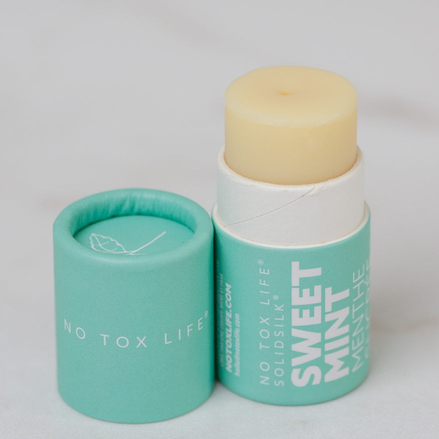 Balm with a green container labeled 'No Tox Life' on a light gray background