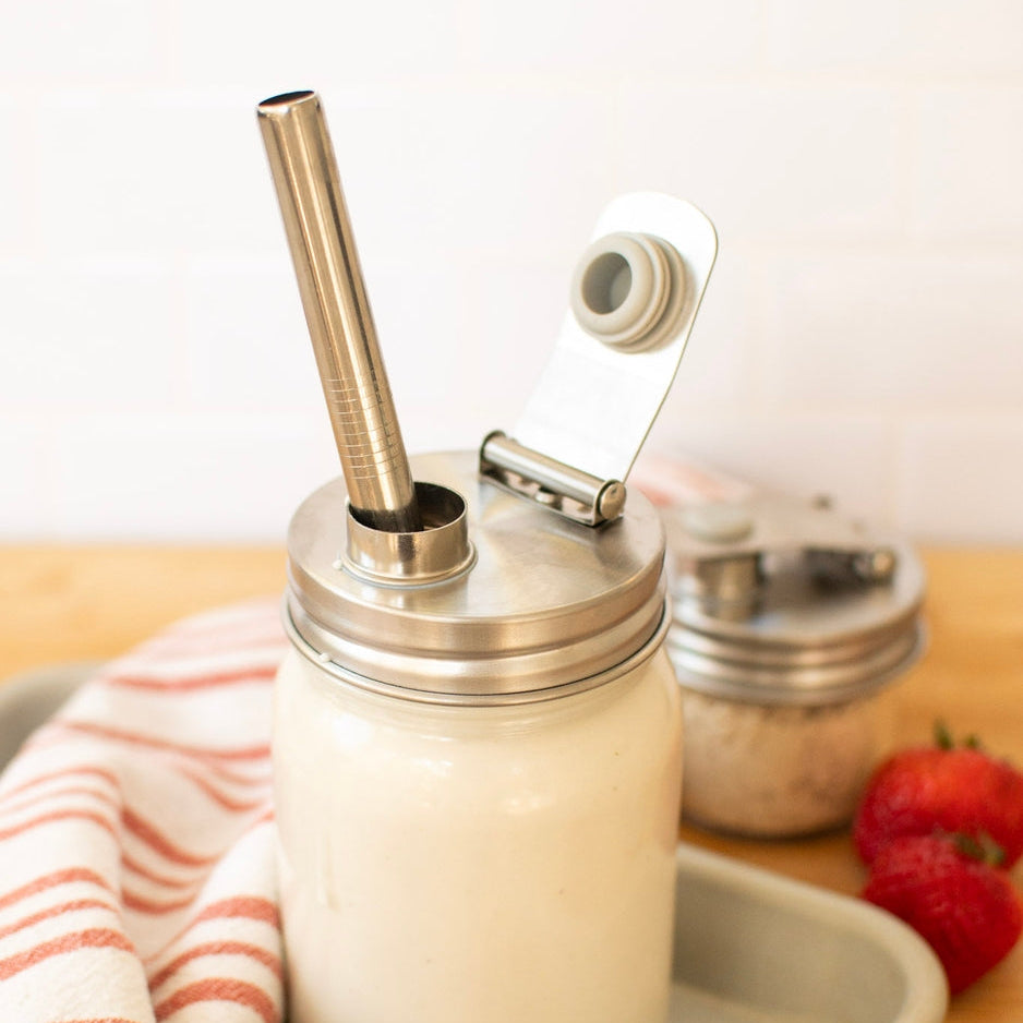Glass jar with metal lid and straw on a tray with strawberries