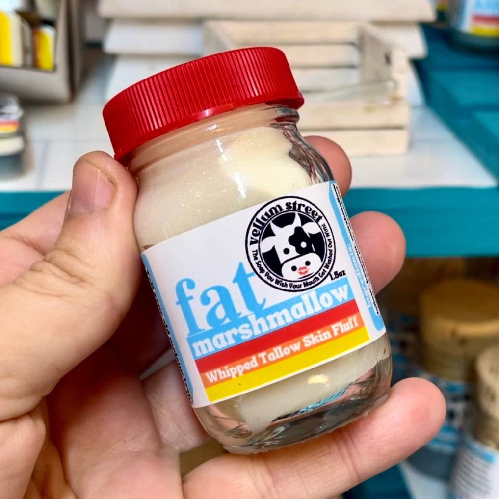 Hand holding a jar of Yelm Street fat marshmallow whipped tallow skin fluff with a red lid.