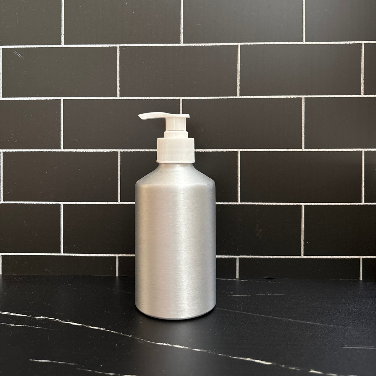 Aluminum bottle with a pump against a black tiled wall