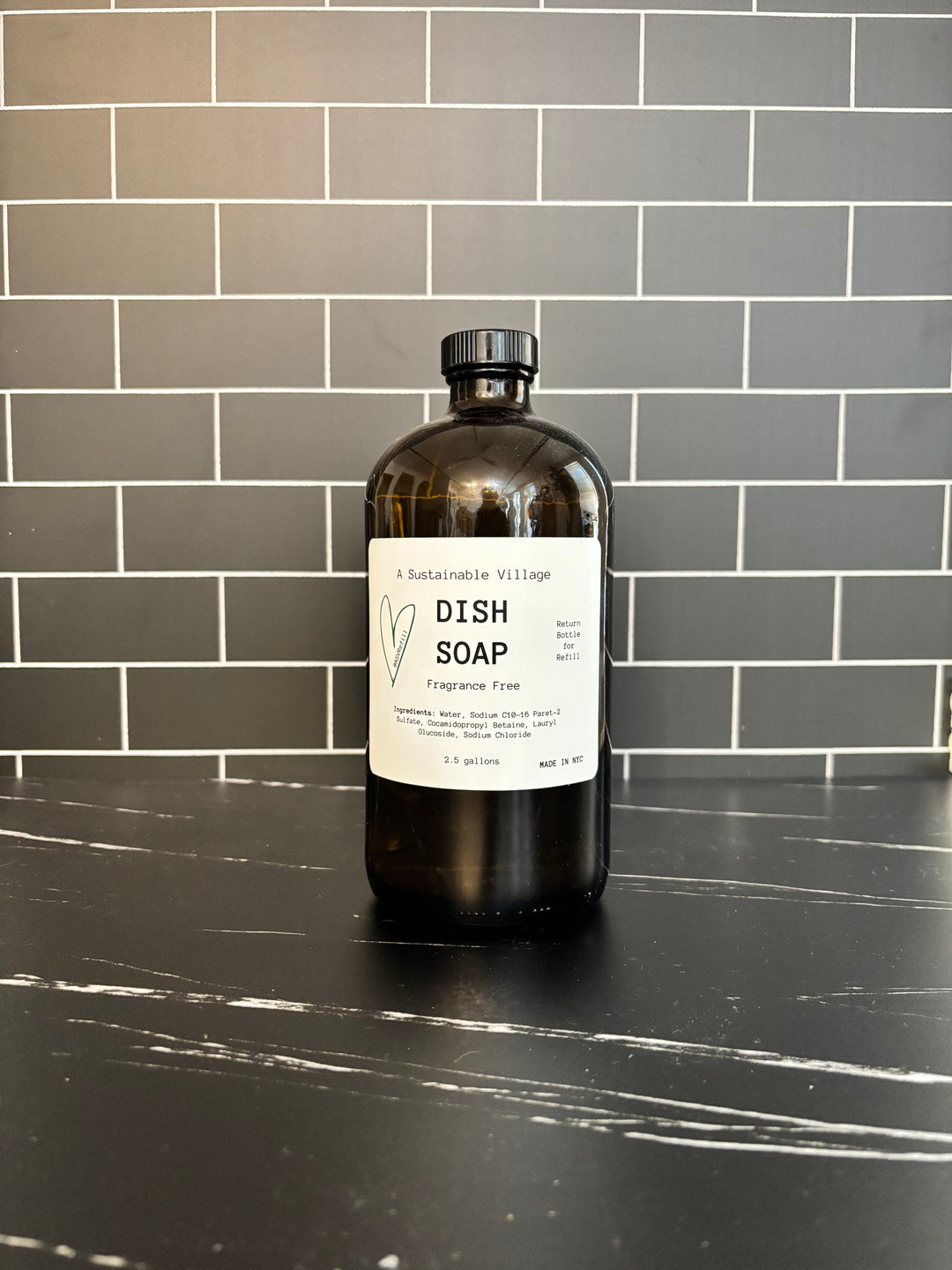 Bottle of dish soap on a black countertop with a tiled wall background refill zero waste plastic free glass bottle 32 oz