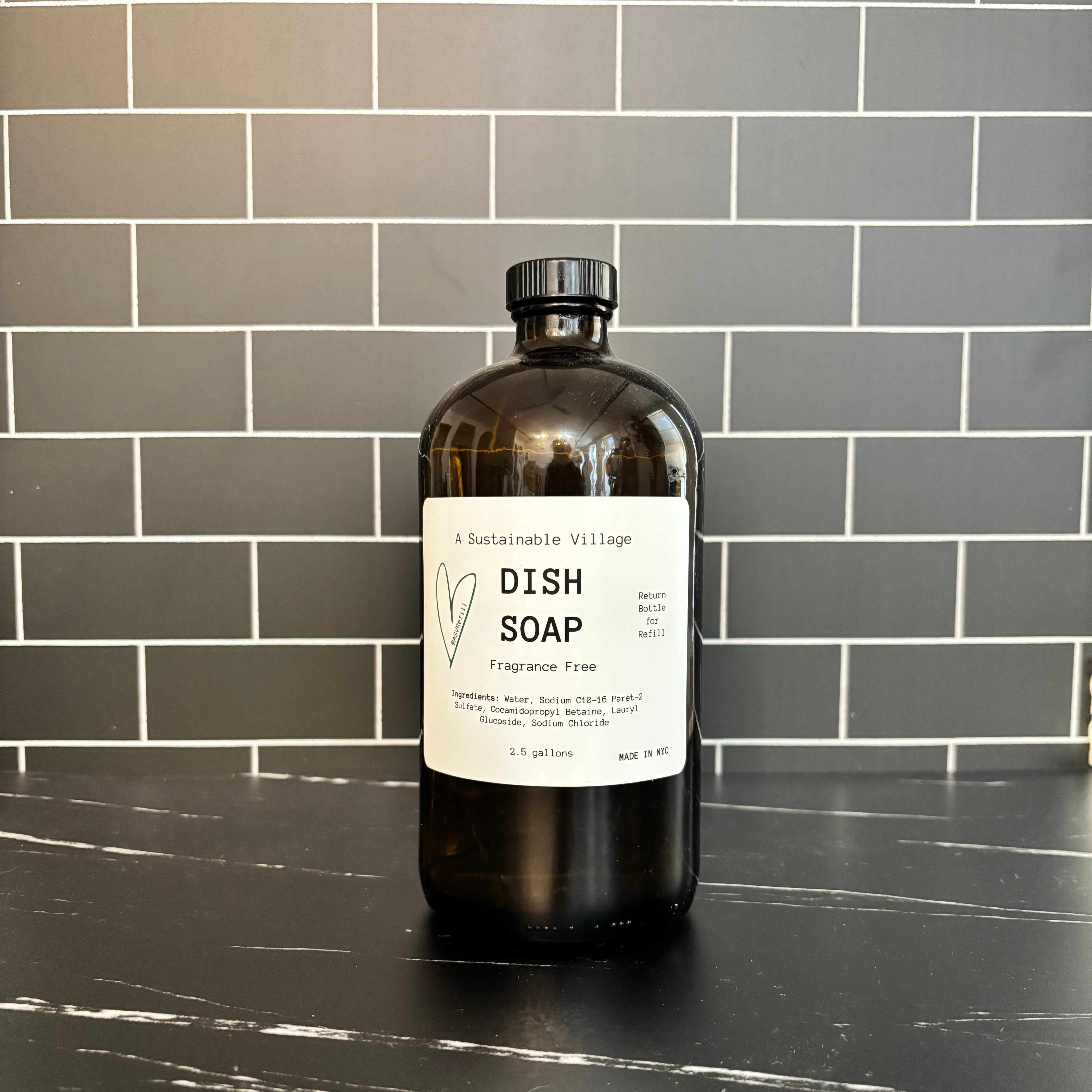 Bottle of dish soap on a black countertop with a tiled wall background refill zero waste plastic free glass bottle 32 oz