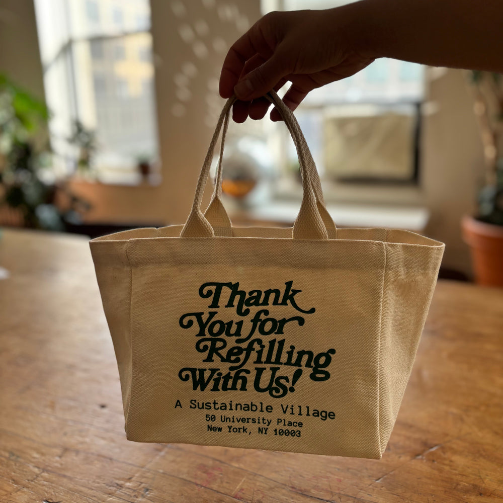 Beige tote bag with text held by a hand on a wooden surface