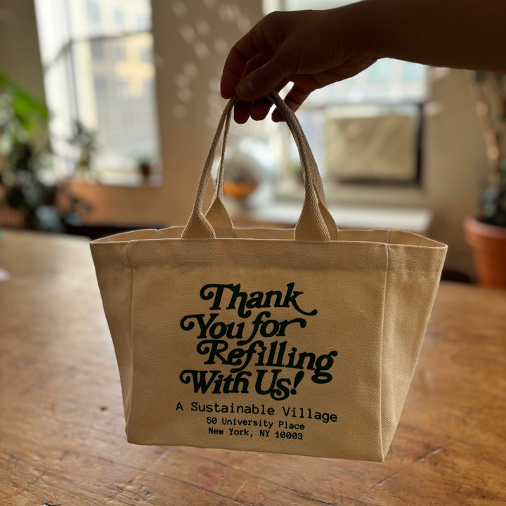 Beige tote bag with text held by a hand on a wooden surface