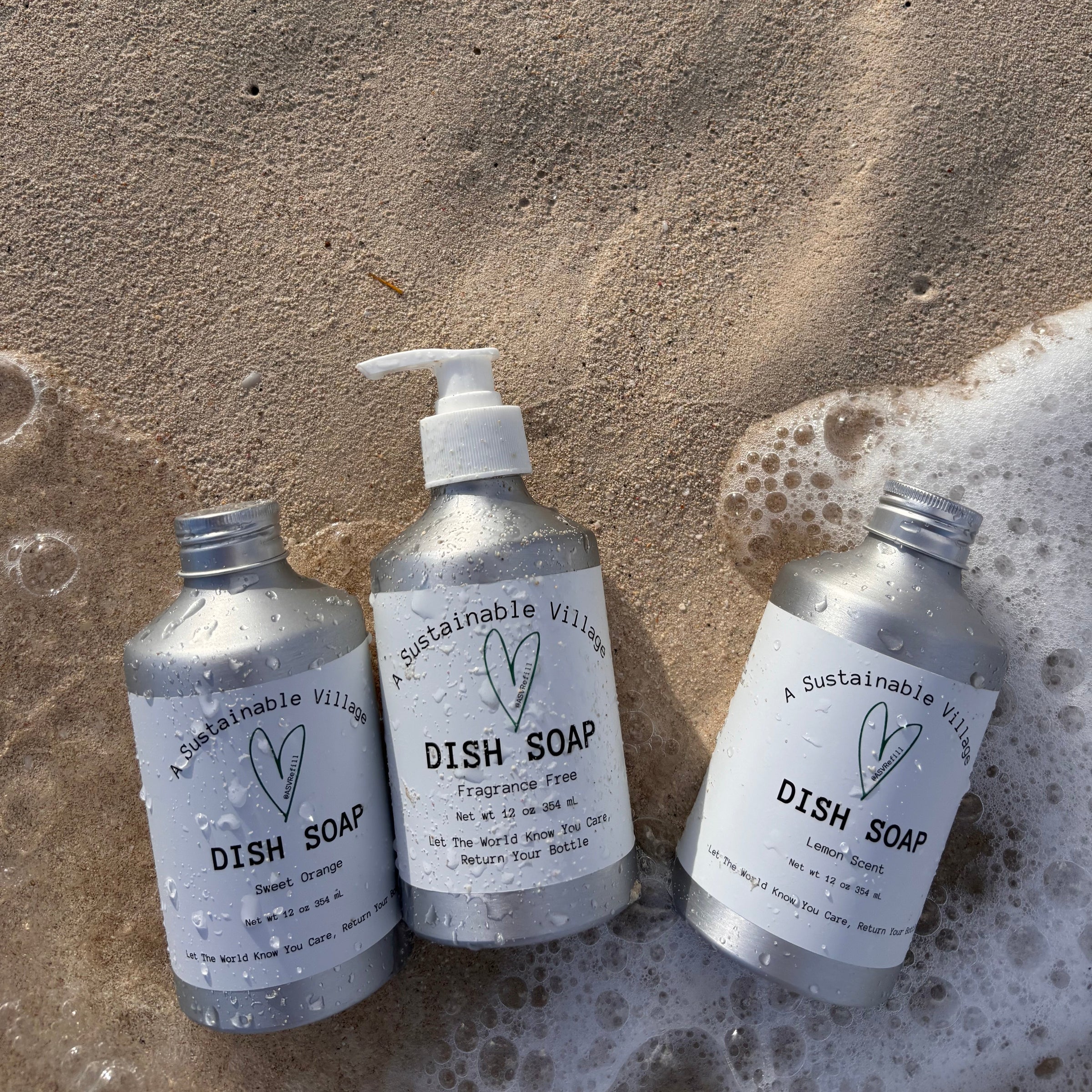 Three bottles of dish soap on a sandy surface with bubbles.