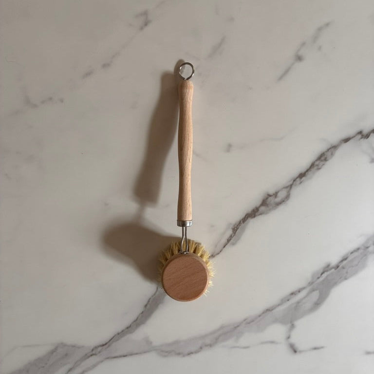 Natural dishwashing brush with wooden handle on a marble surface for a plastic free kitchen