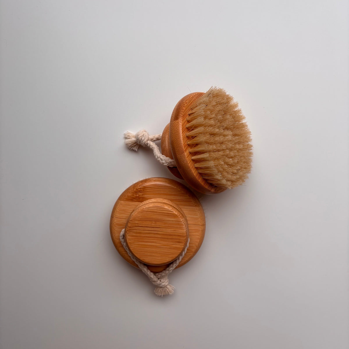 Two wooden body brushes with natural bristles and rope handles, shown on a plain light gray background.