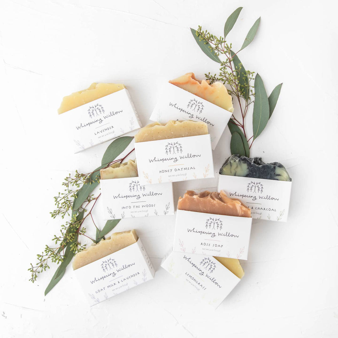 Bar soaps from Whispering Willow with a gentle yellow color, displayed on a white surface with green leaves and packaging.