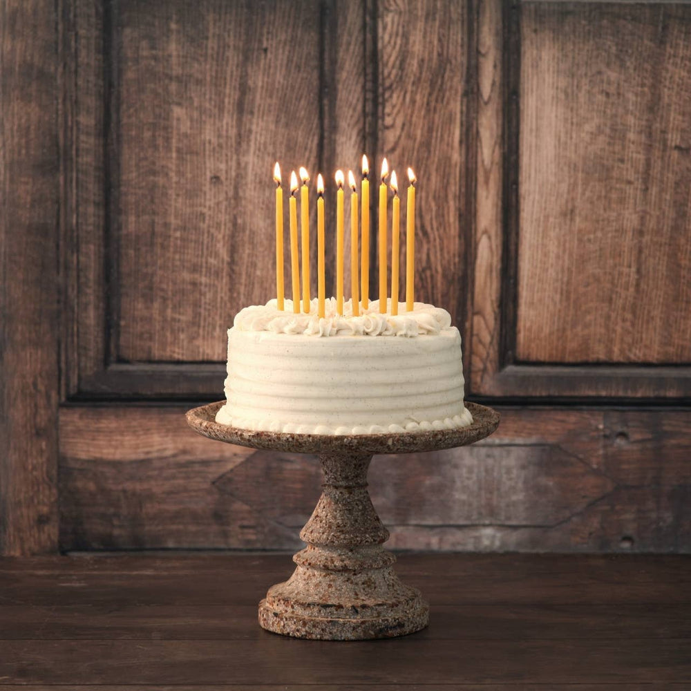 White cake with lit candles on a rustic stand against a wooden background