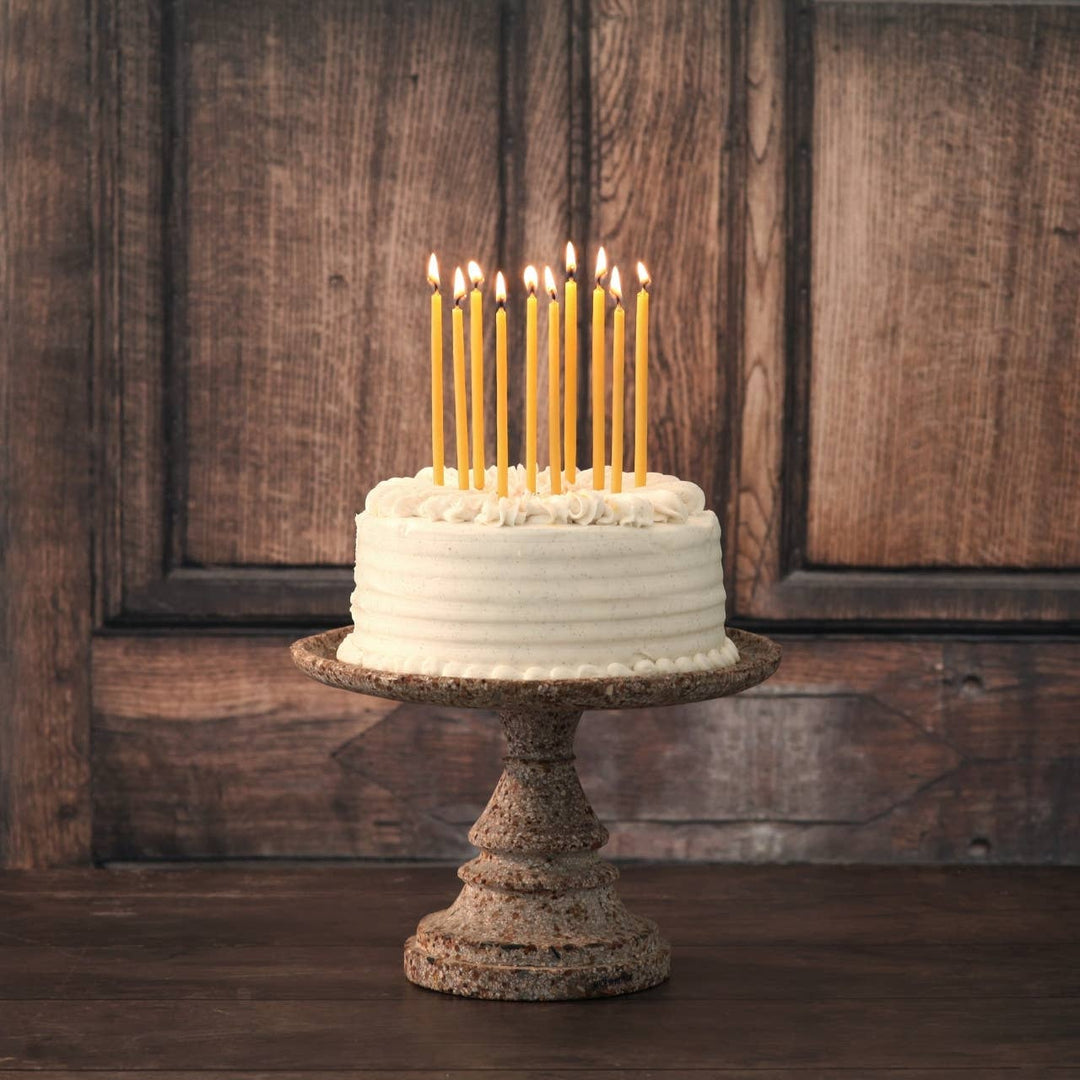 White cake with lit candles on a rustic stand against a wooden background