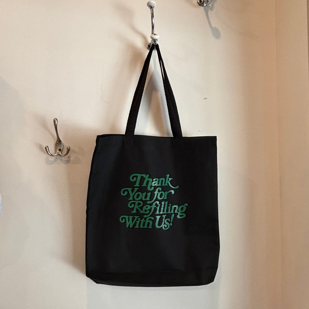 Black tote bag with green text hanging on a wall hook.