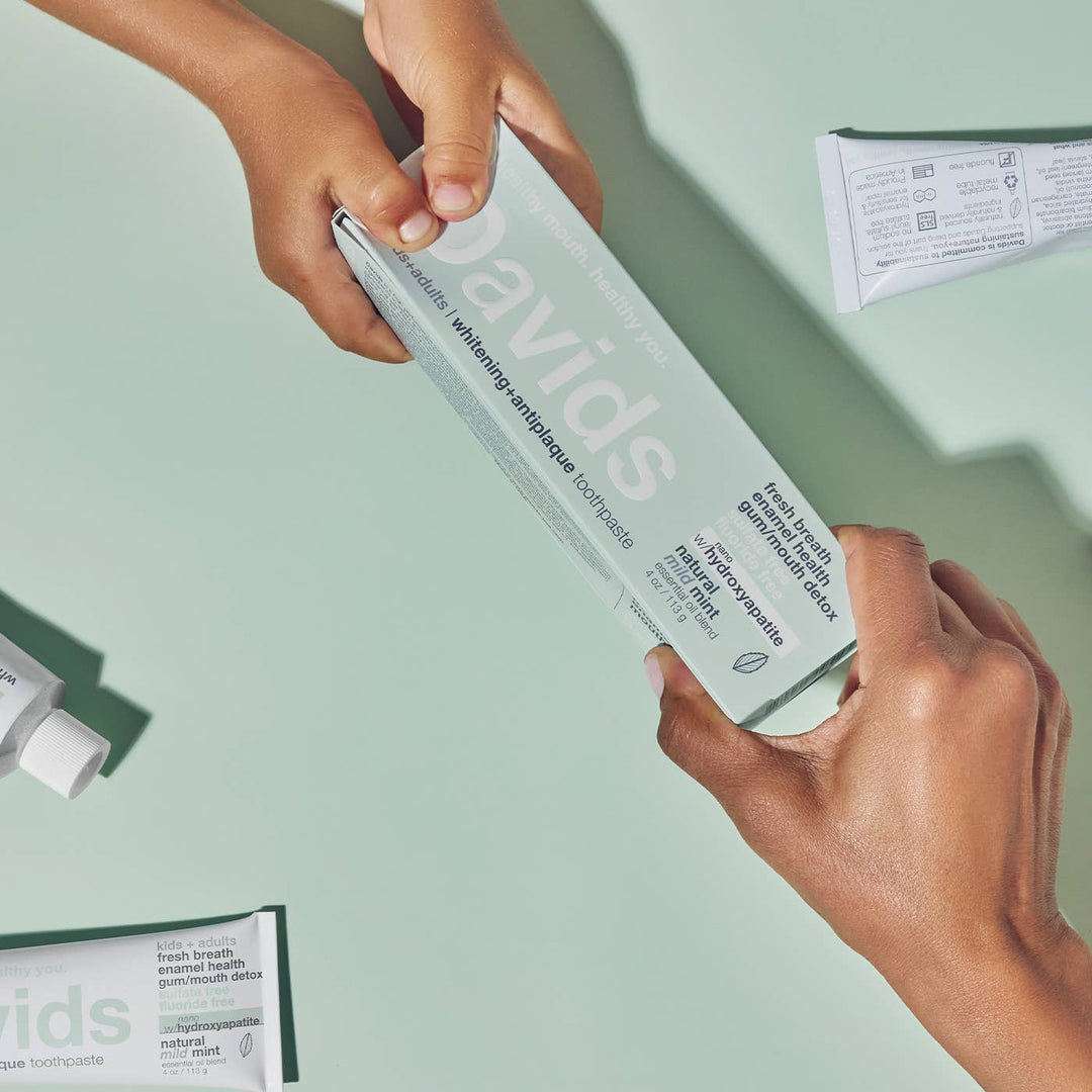 Two hands holding a box of Davids toothpaste against a light green background