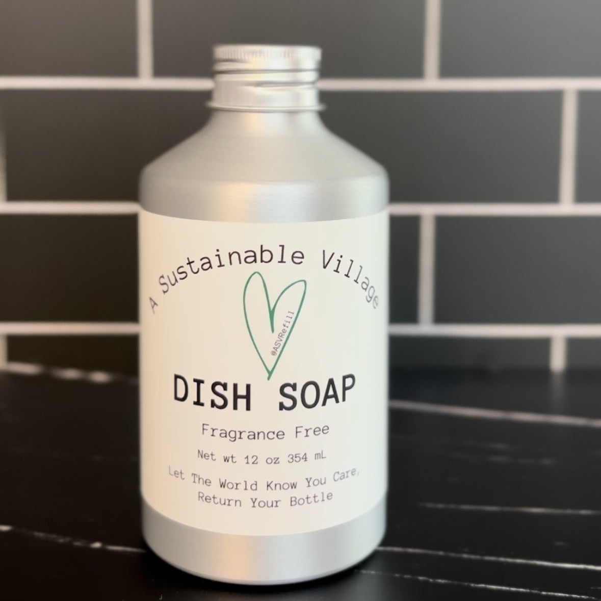 Bottle of A Sustainable Village refill dish soap on a black surface with a tiled wall background plastic free aluminum bottle