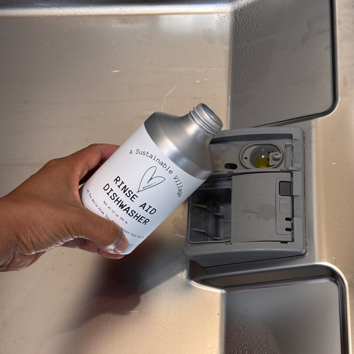 Hand holding a bottle labeled 'Rings A10 Dishwasher' above a metallic surface.