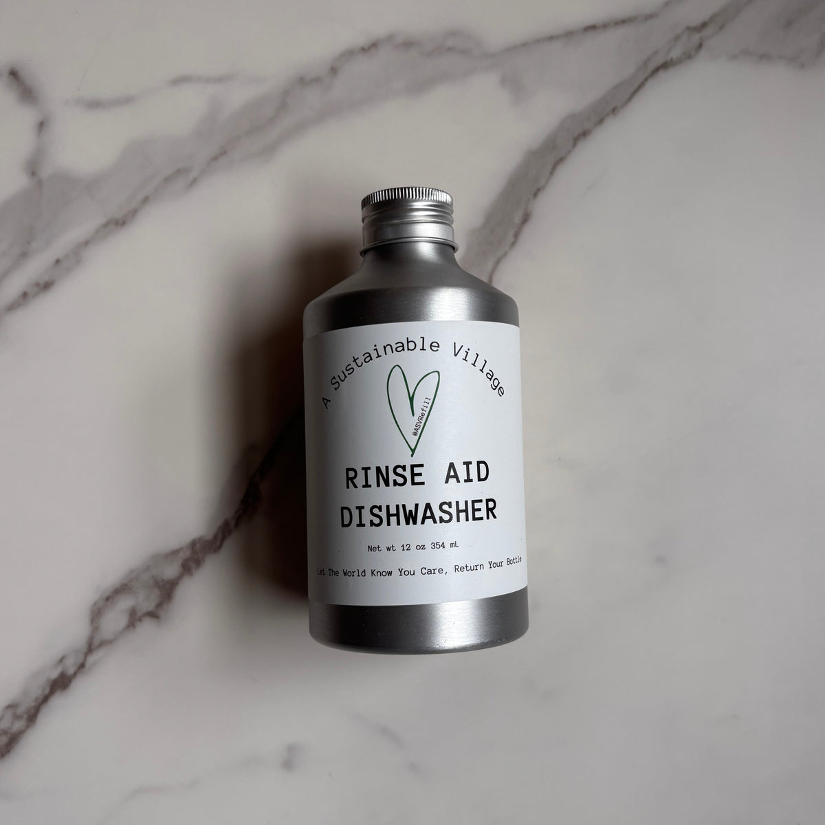 Bottle of Sustainable Village Rinse Aid Dishwasher on a marble surface 12 oz refillable in aluminum bottle