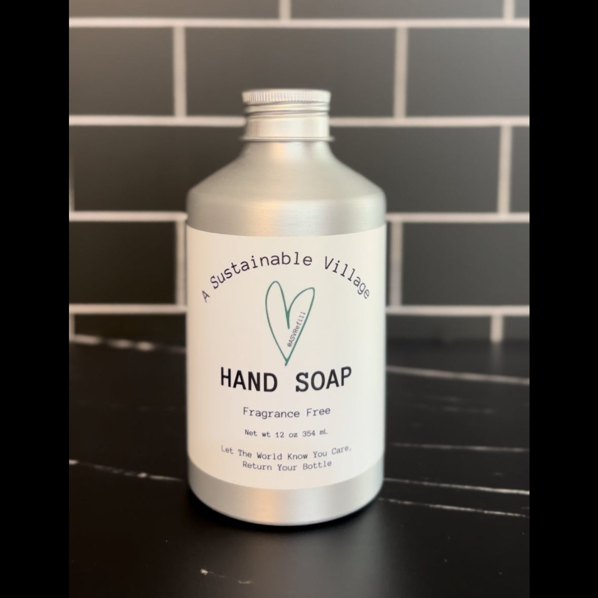 Fragrance Free Hand soap bottle with 'Sustainable Village' label on a tiled wall background plastic free