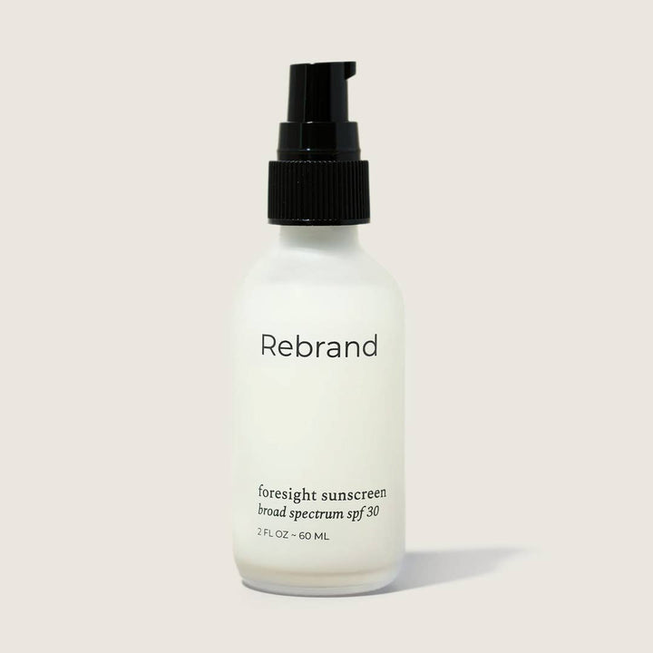 Sunscreen bottle labeled 'Rebrand' on a light background