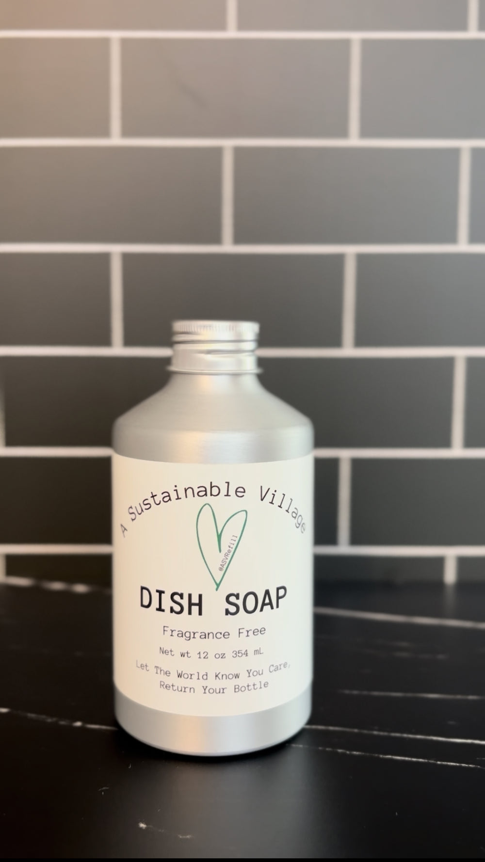 Bottle of A Sustainable Village refill dish soap on a black surface with a tiled wall background plastic free aluminum bottle