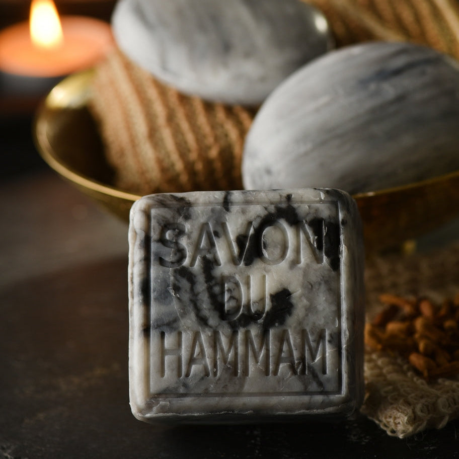 Bar of Savon du Hammam soap with two stones and a basket in the background.