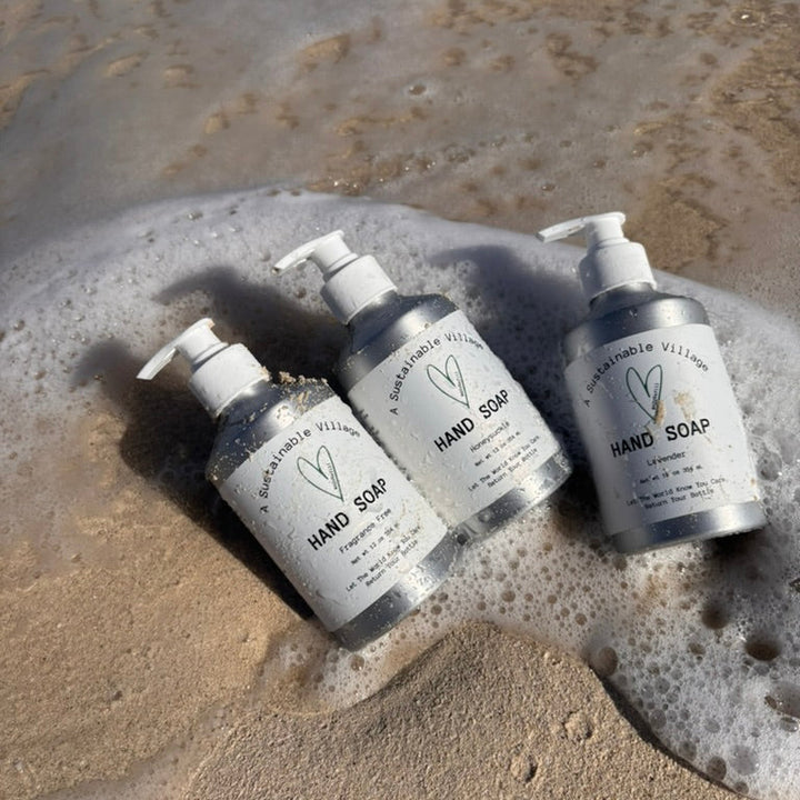 aluminum bottles of hand soap on a sandy surface with water and foam.