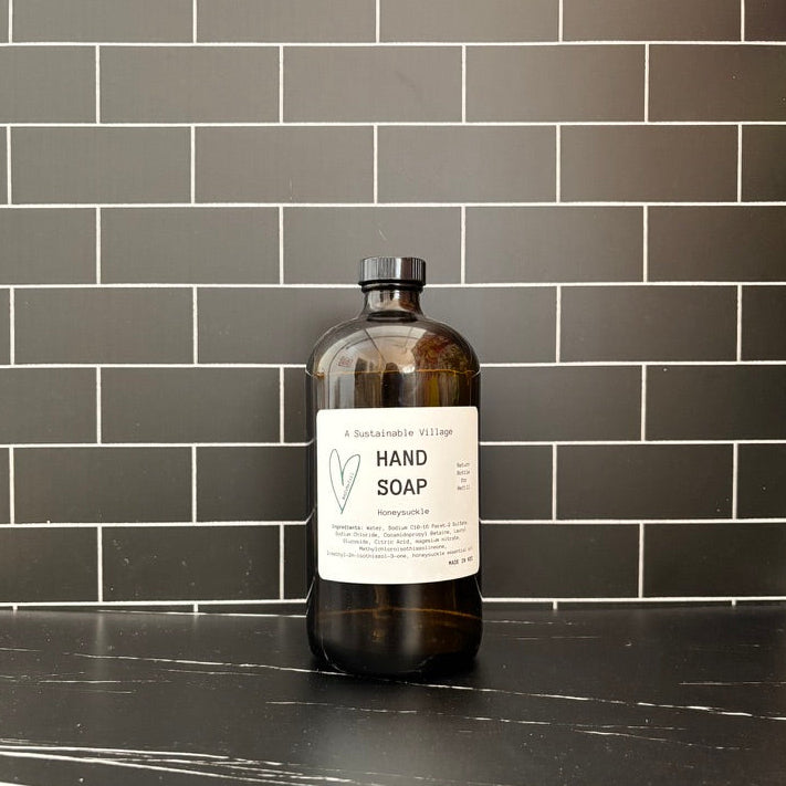 Amber glass hand soap bottle with a label on a black countertop against a gray tiled wall.