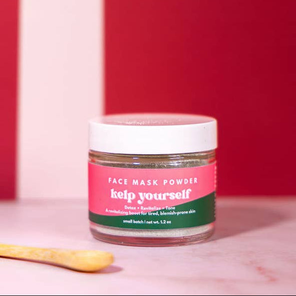 Jar of face mask powder with a wooden spoon on a pink background