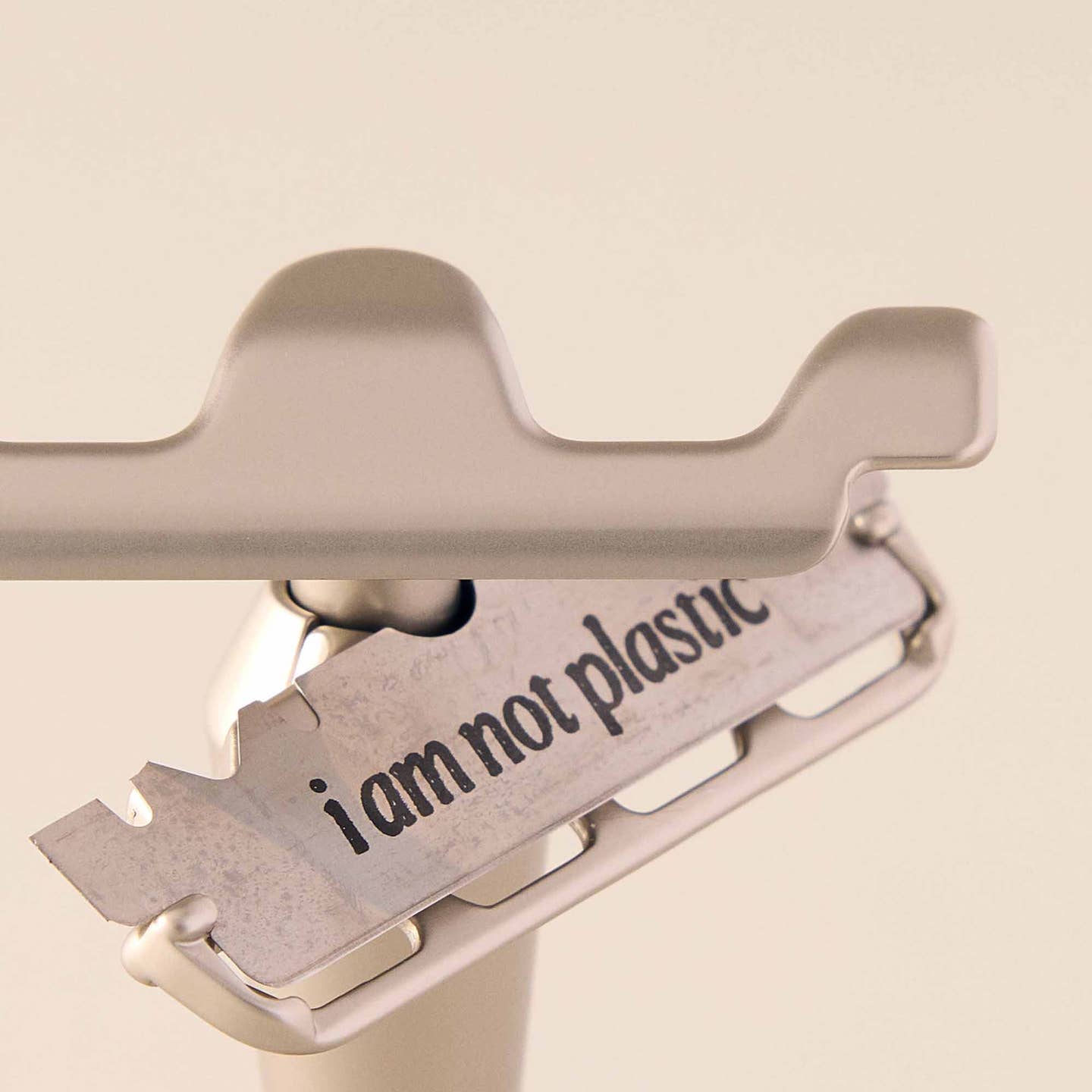 Metallic razor blade with 'i am not plastic' text on a beige background