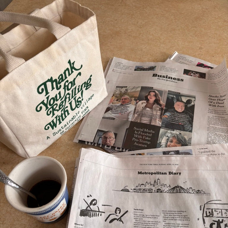 Newspaper with a hand holding it, a cup of coffee, and a tote bag with text on a table.