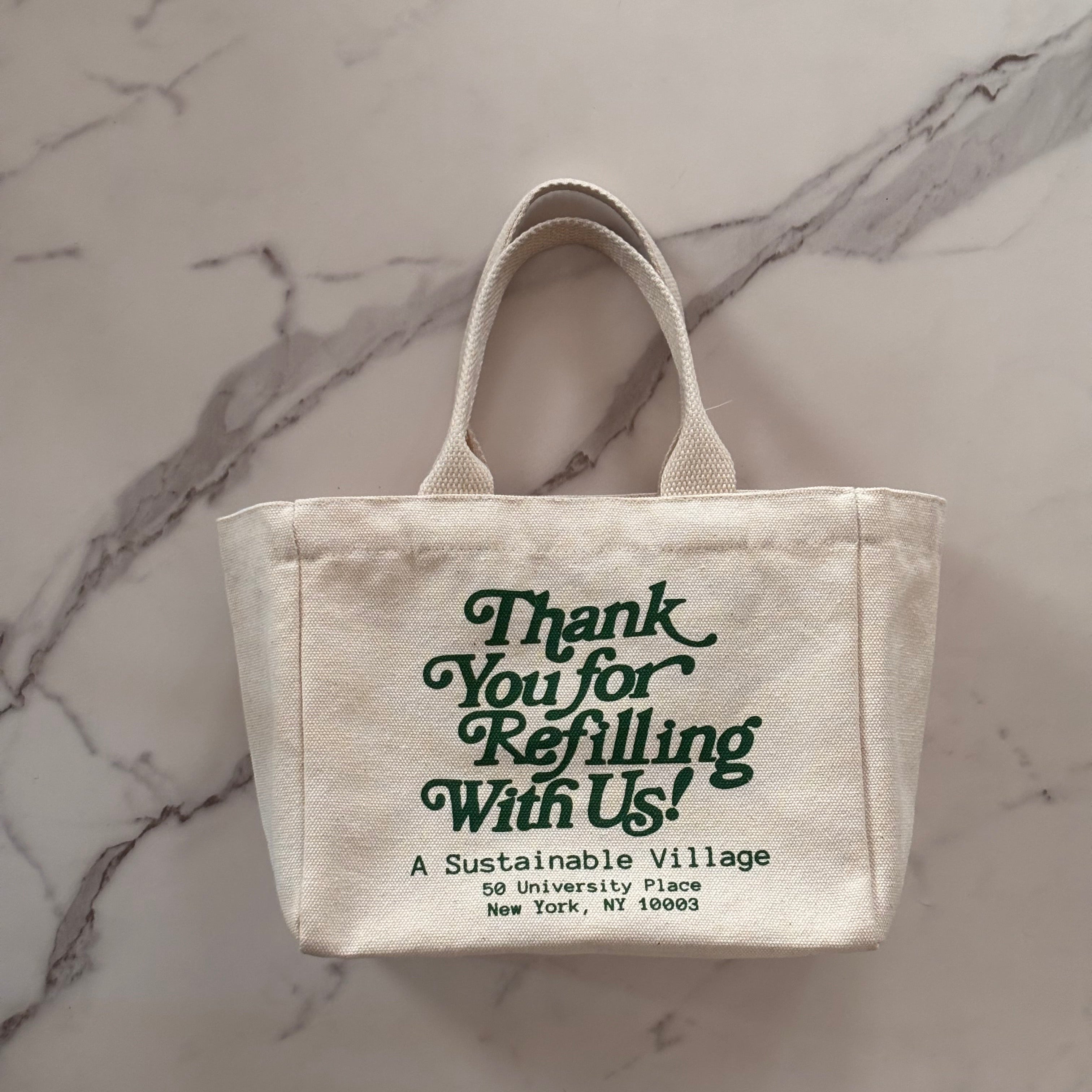 Small beige tote bag with green text on a marble surface