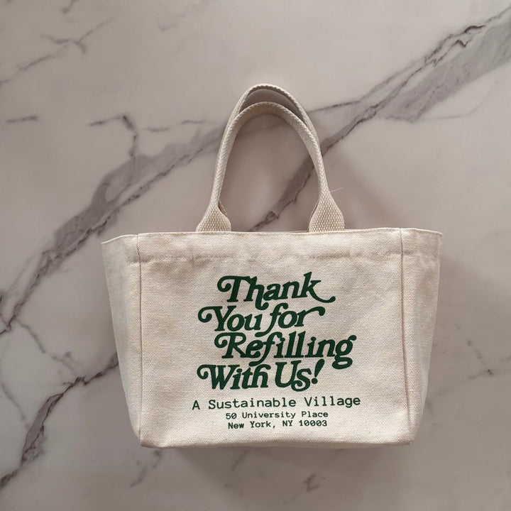 Small beige tote bag with green text on a marble surface