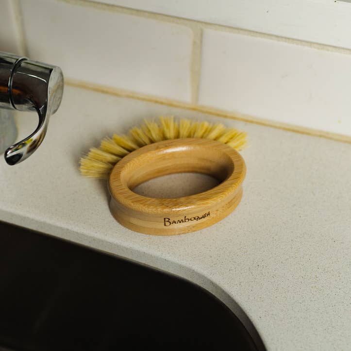 A bamboo dish brush with yellow bristles resting on a kitchen counter.