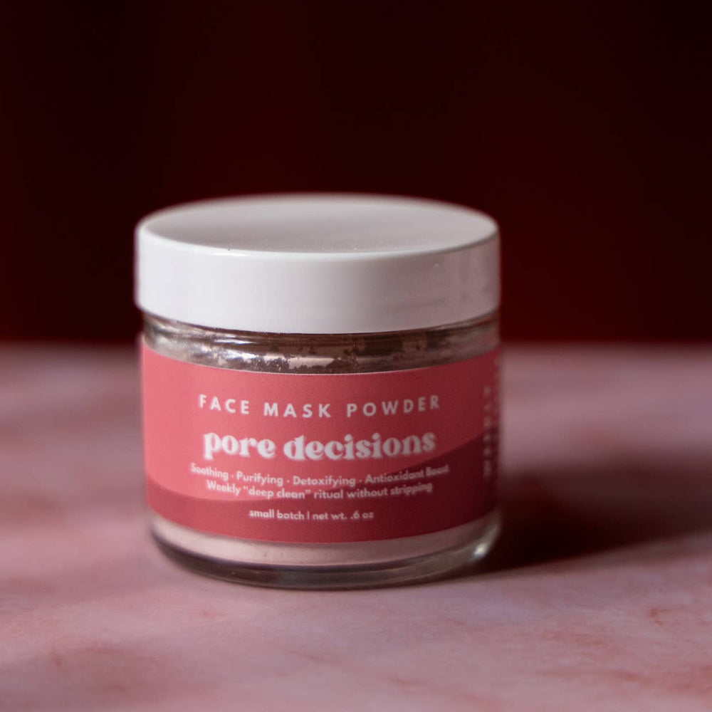 Jar of 'Pore Decisions' face mask powder on a textured surface with a dark background