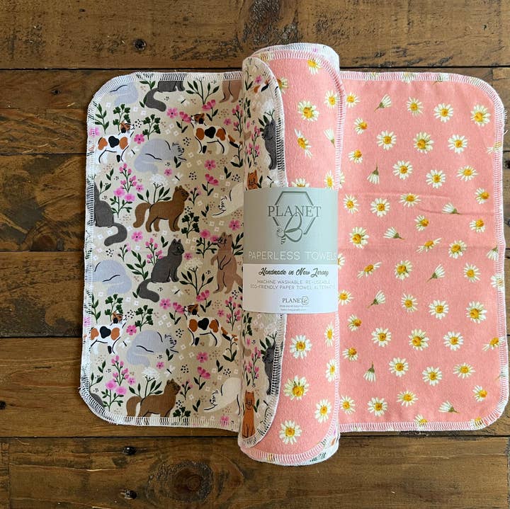 Two burp cloths with animal pattern and floral design on a wooden surface, featuring a Planet Burpless Towels label.