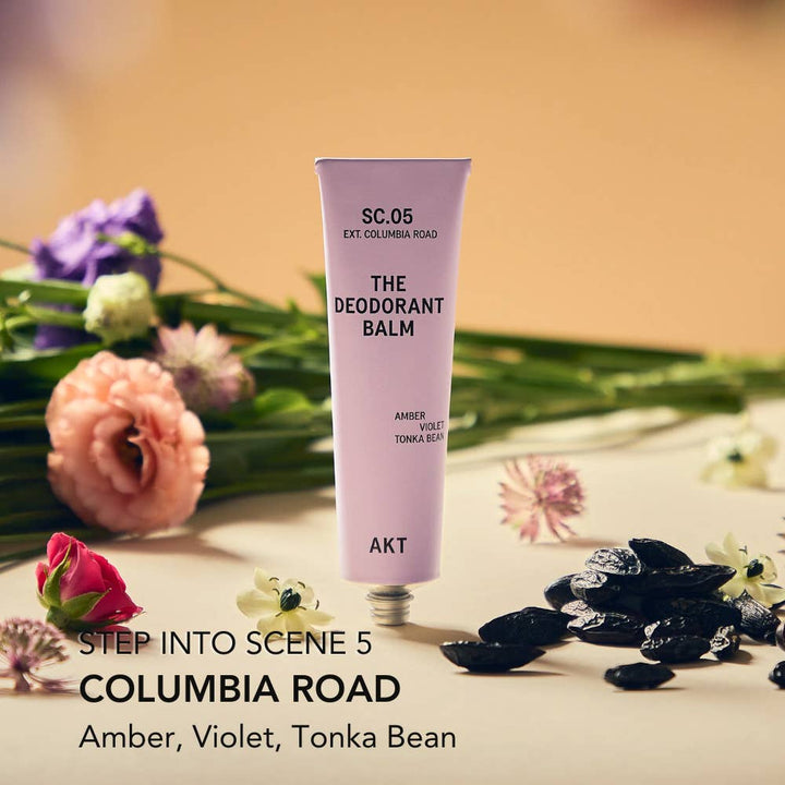 Deodorant balm tube labeled 'SC.05 The Deodorant Balm' with flowers and black stones on a wooden surface. Plastic free.  Zero waste