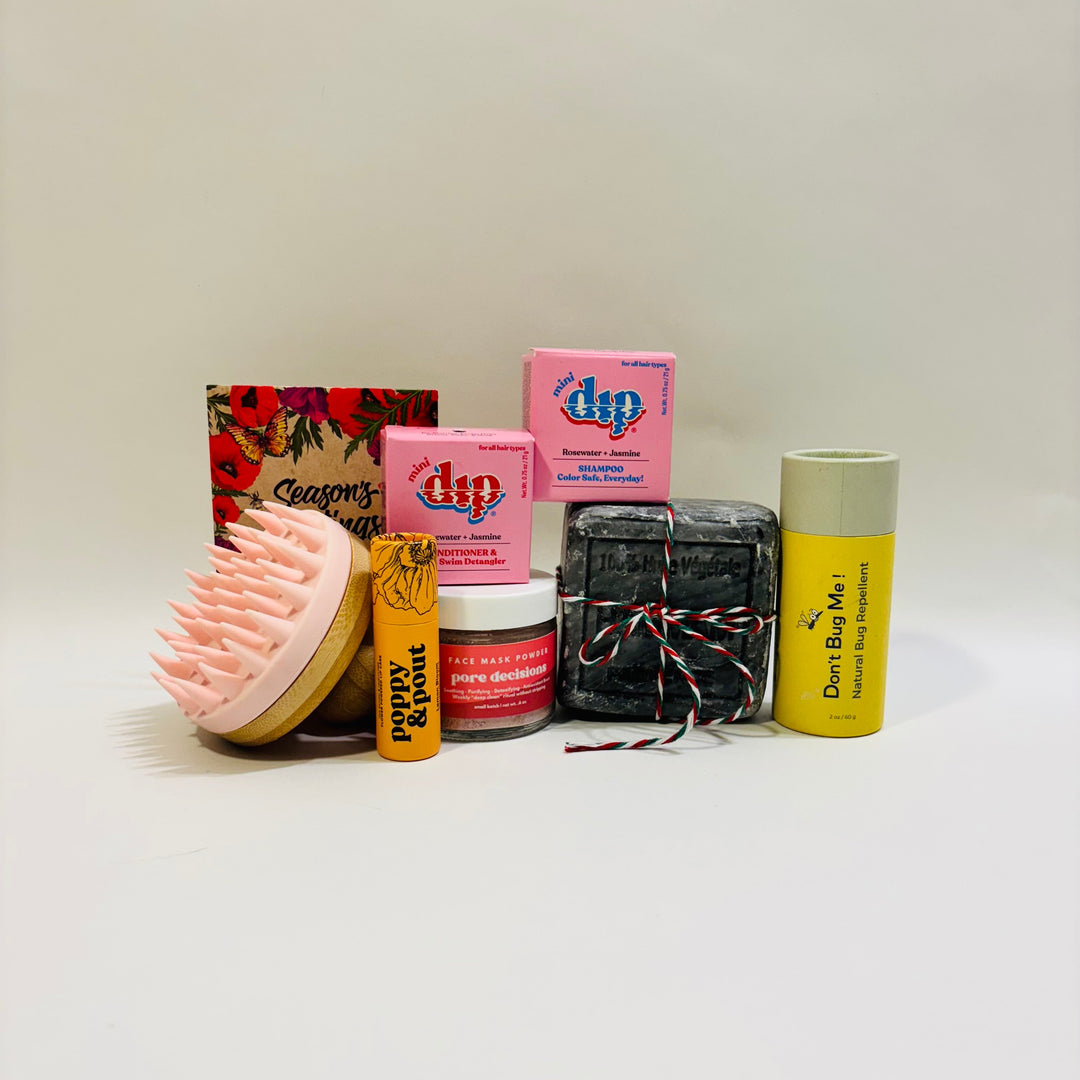 Collection of beauty products including a mini Dip Shampoo, mini Dip Conditioner, a Scalp Massager, face mask by Barely Serious, Don't Buy Me insect repellant by Oliver Flynn, lip balm by Poppy & Poppy and a packet of flower seeds.