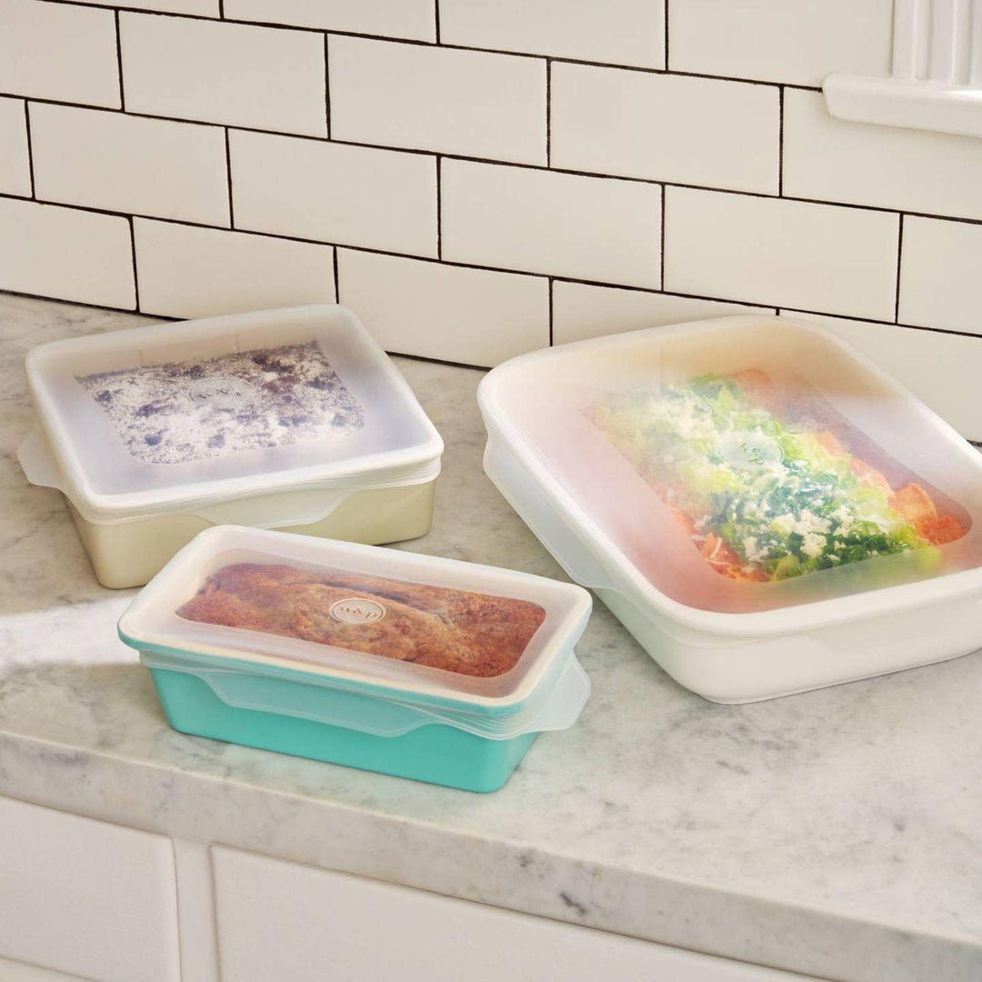 Three silicone food containers with different colored lids on a kitchen counter.