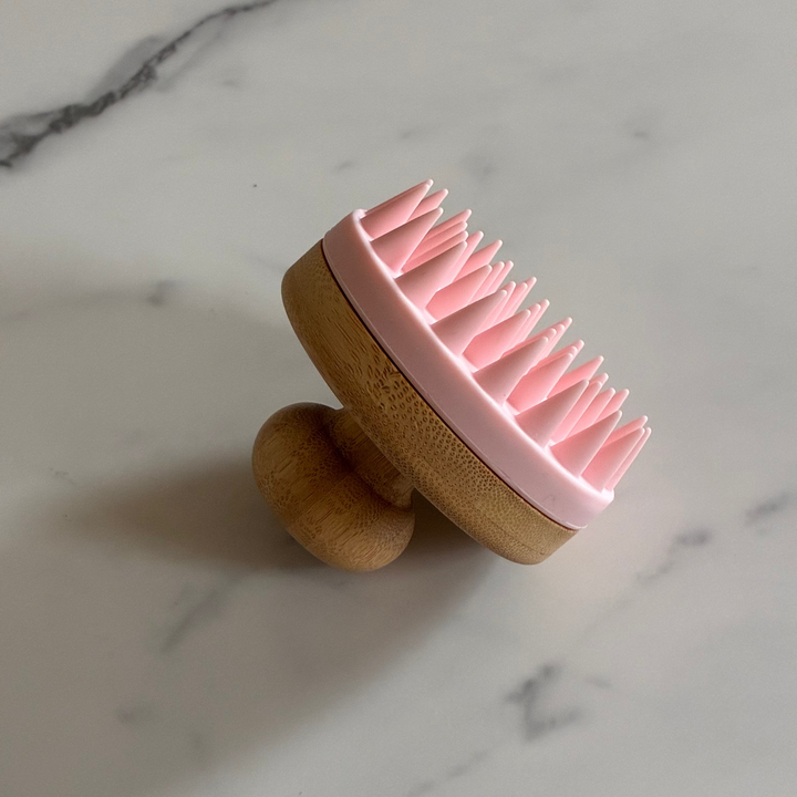 Silicone scalp massager with wooden handle on a marble surface