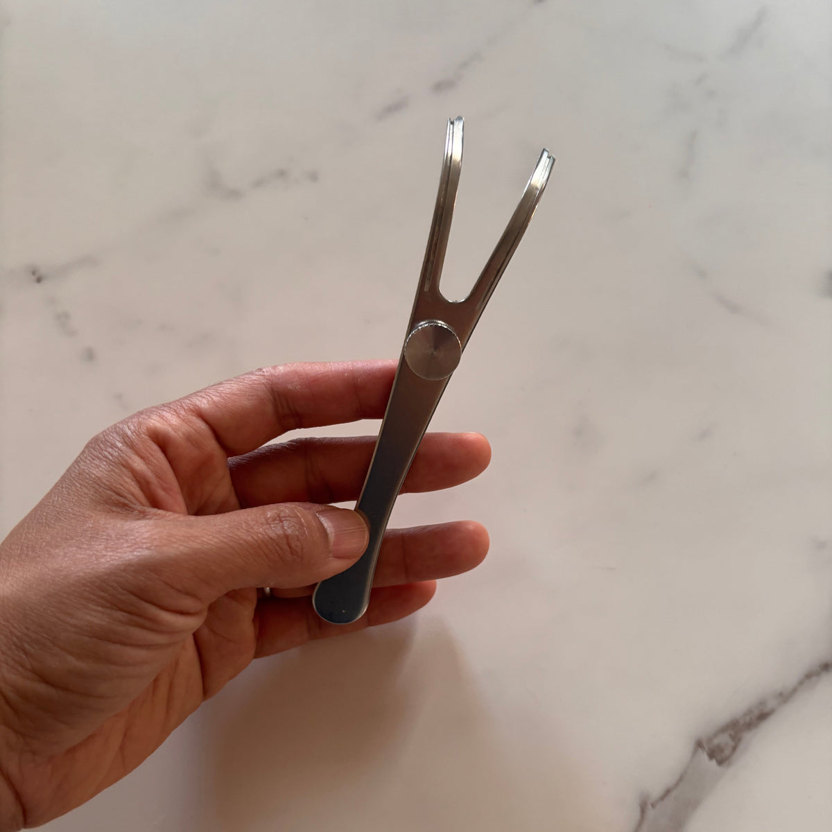 Hand holding a Dental Lace Stainless Steel Refillable Flosser against a marble background