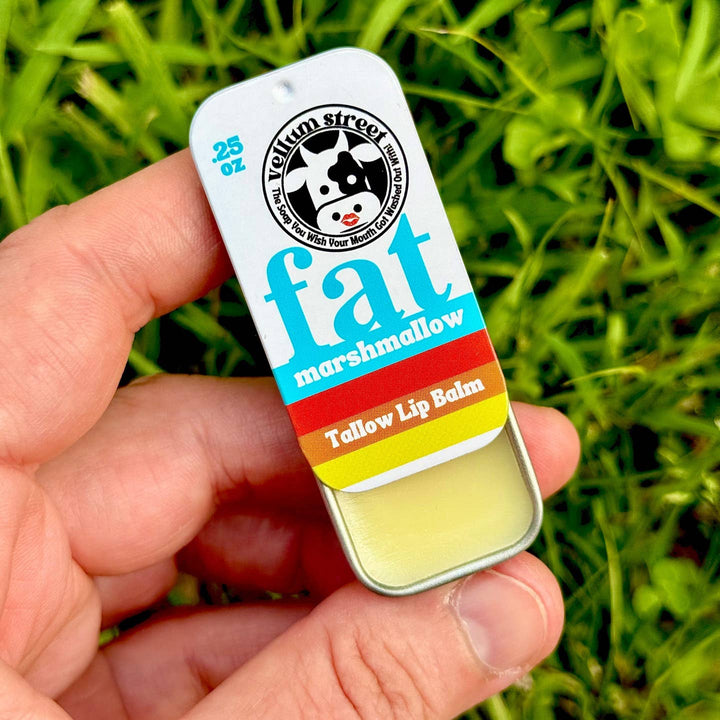 Hand holding a lip balm with a colorful label against a grassy background